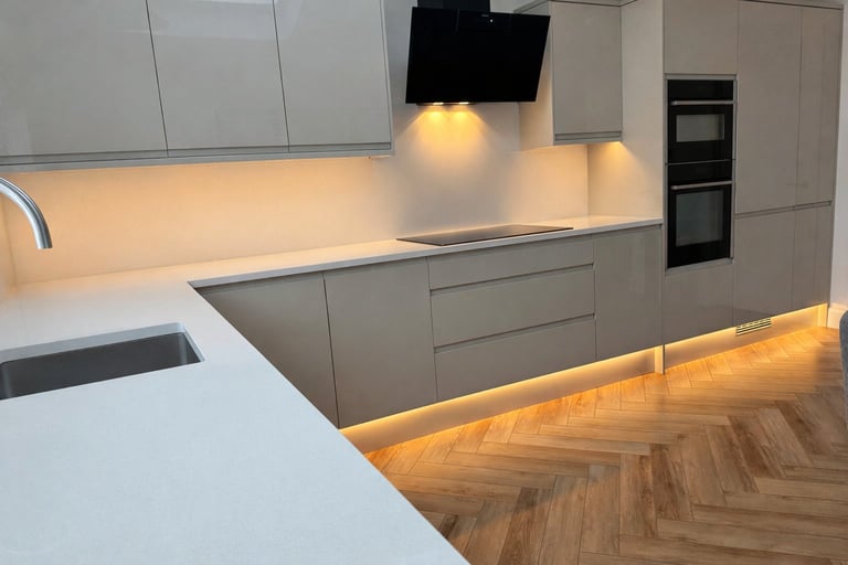 Modern kitchen with white and gray cabinetry, black range hood, undermount lighting, and herringbone wood flooring