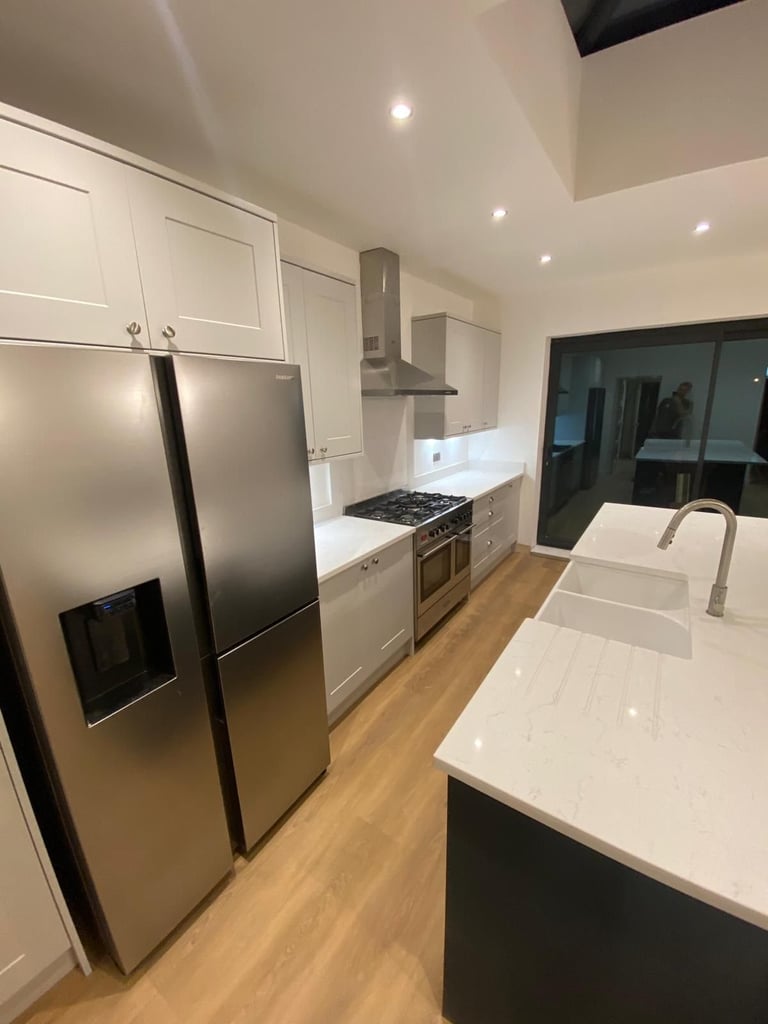 Modern kitchen with white cabinetry, stainless steel appliances, gas range, white quartz countertops, and wood flooring