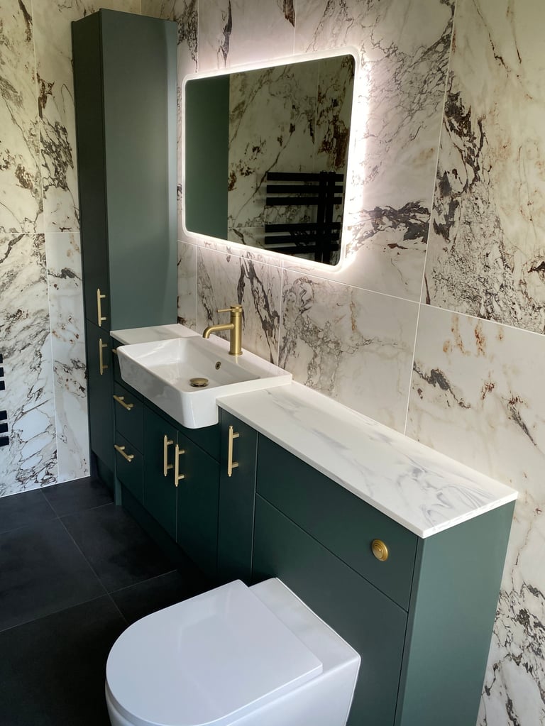 Modern bathroom with green vanity, white sink, illuminated mirror, marble tile walls, and white toilet