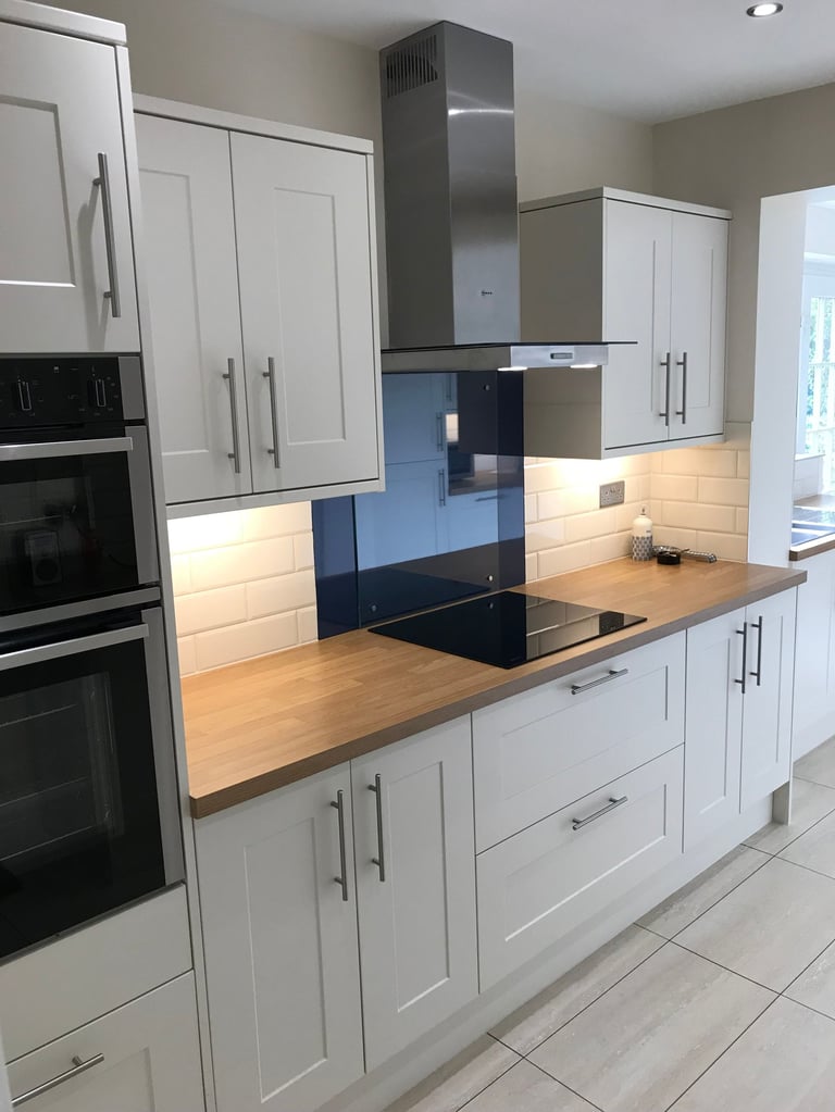 Modern kitchen with white cabinetry, wooden countertops, stainless steel hood, and black glass backsplash