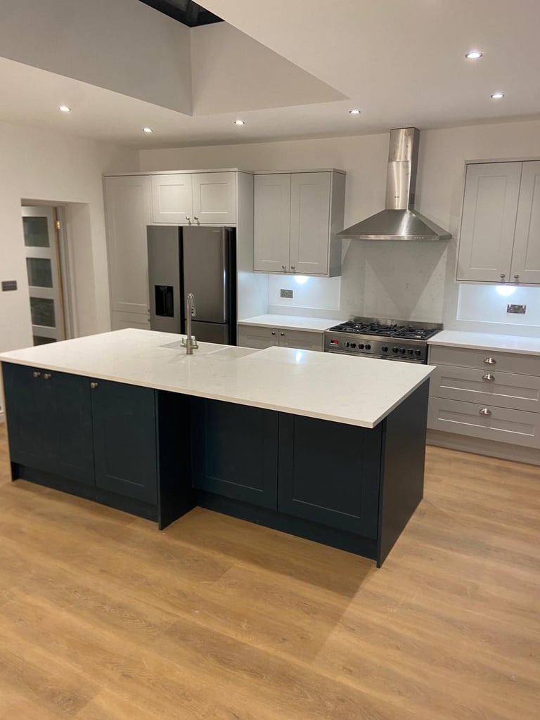 Modern kitchen with white cabinetry, black island with white countertop, stainless steel appliances, and wood flooring